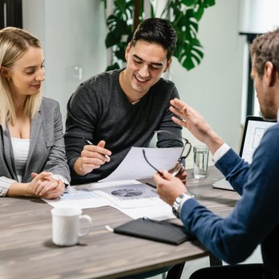 young-happy-couple-reading-terms-of-mortgage-documents-while-having-meeting-with-real-estate-agent-at-home-focus-is-on-young-man