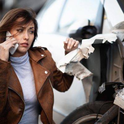 young-sad-woman-using-mobile-phone-and-calling-for-help-while-looking-at-her-wrecked-car